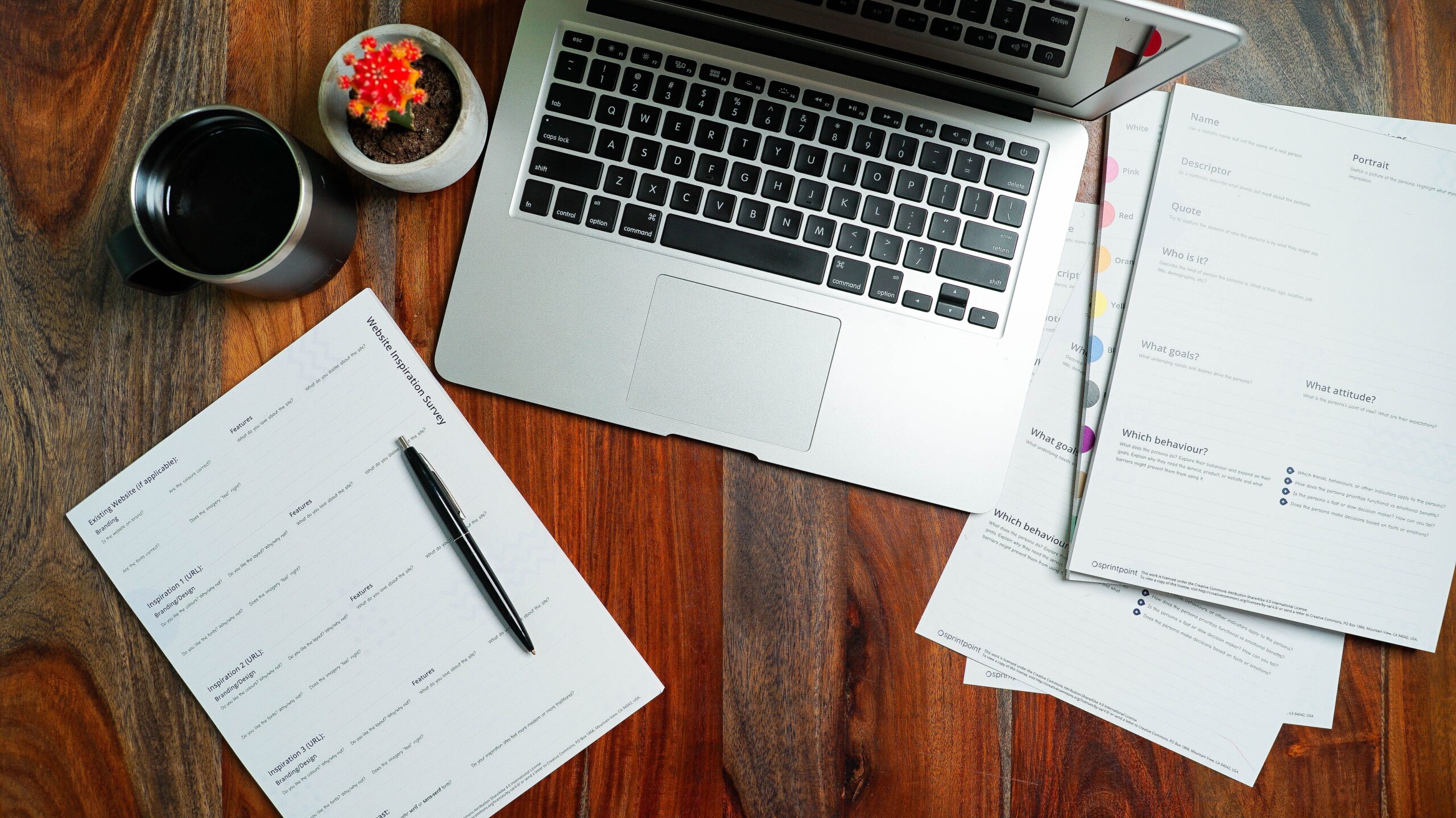 Laptop on wooden table surrounded by paperwork