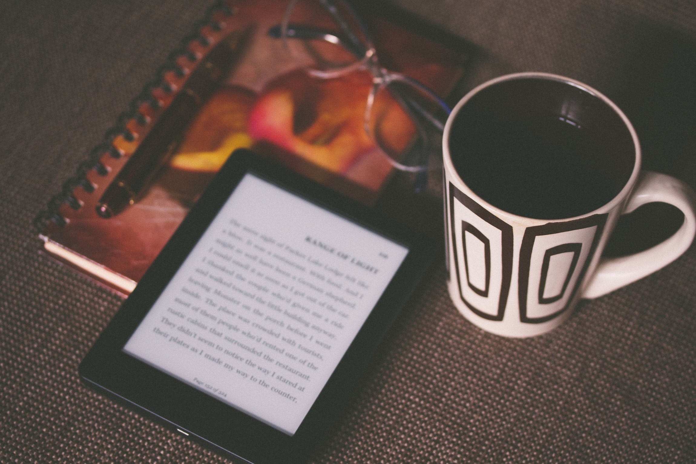ebook reader on table next to mug and notebook