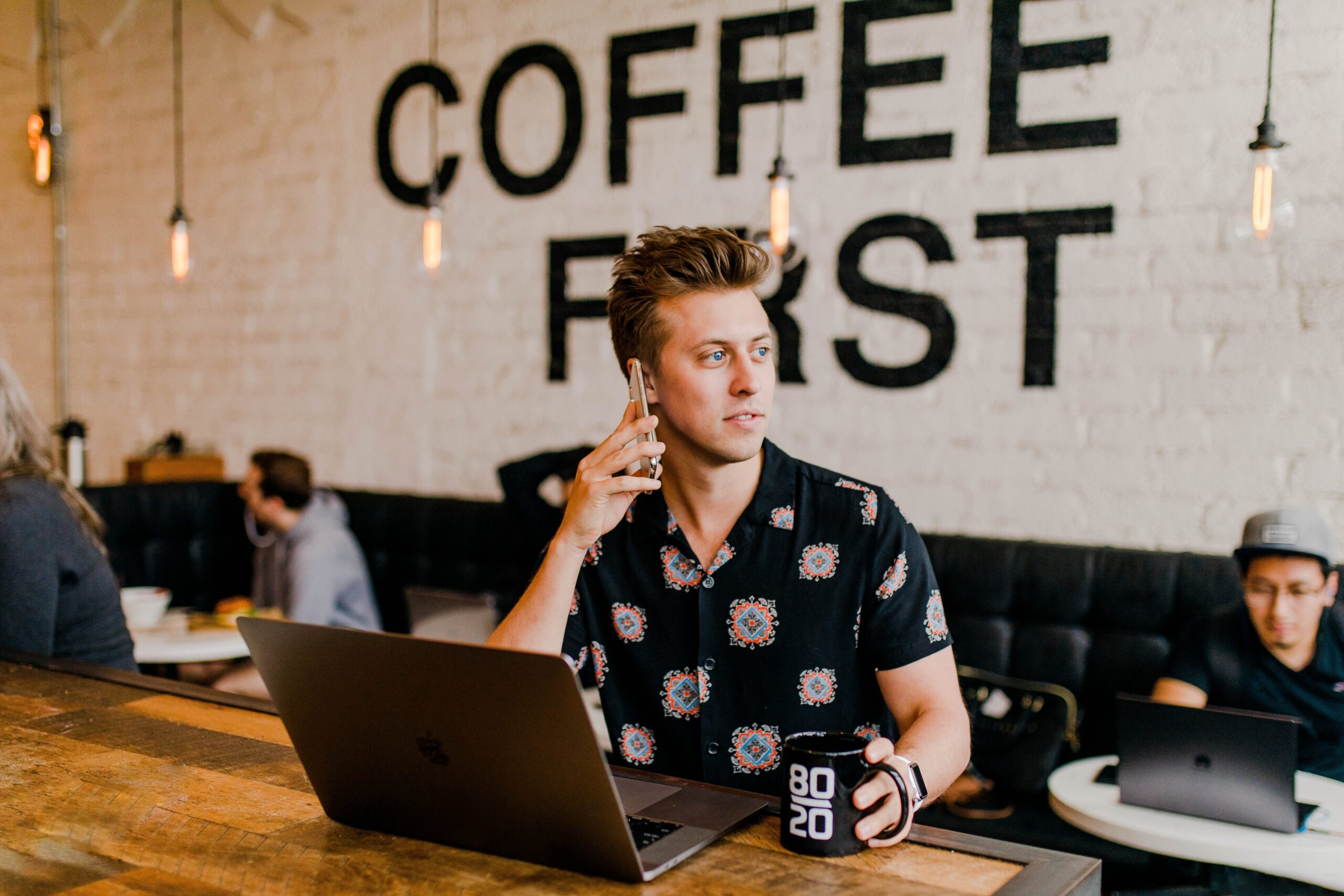 man sitting in a coffee shop on his phone and working on laptop