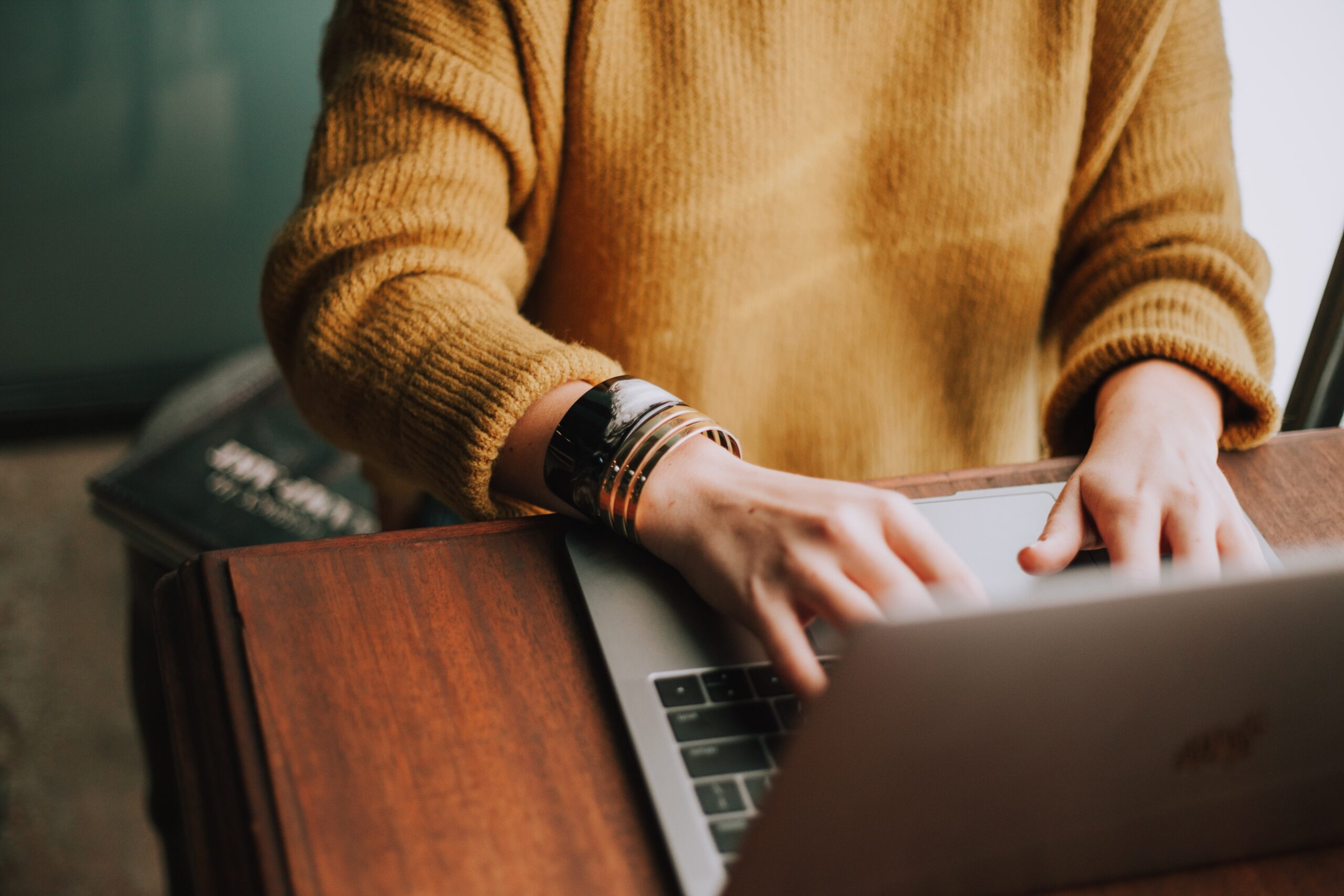 Woman in yellow sweater typing on MacBook