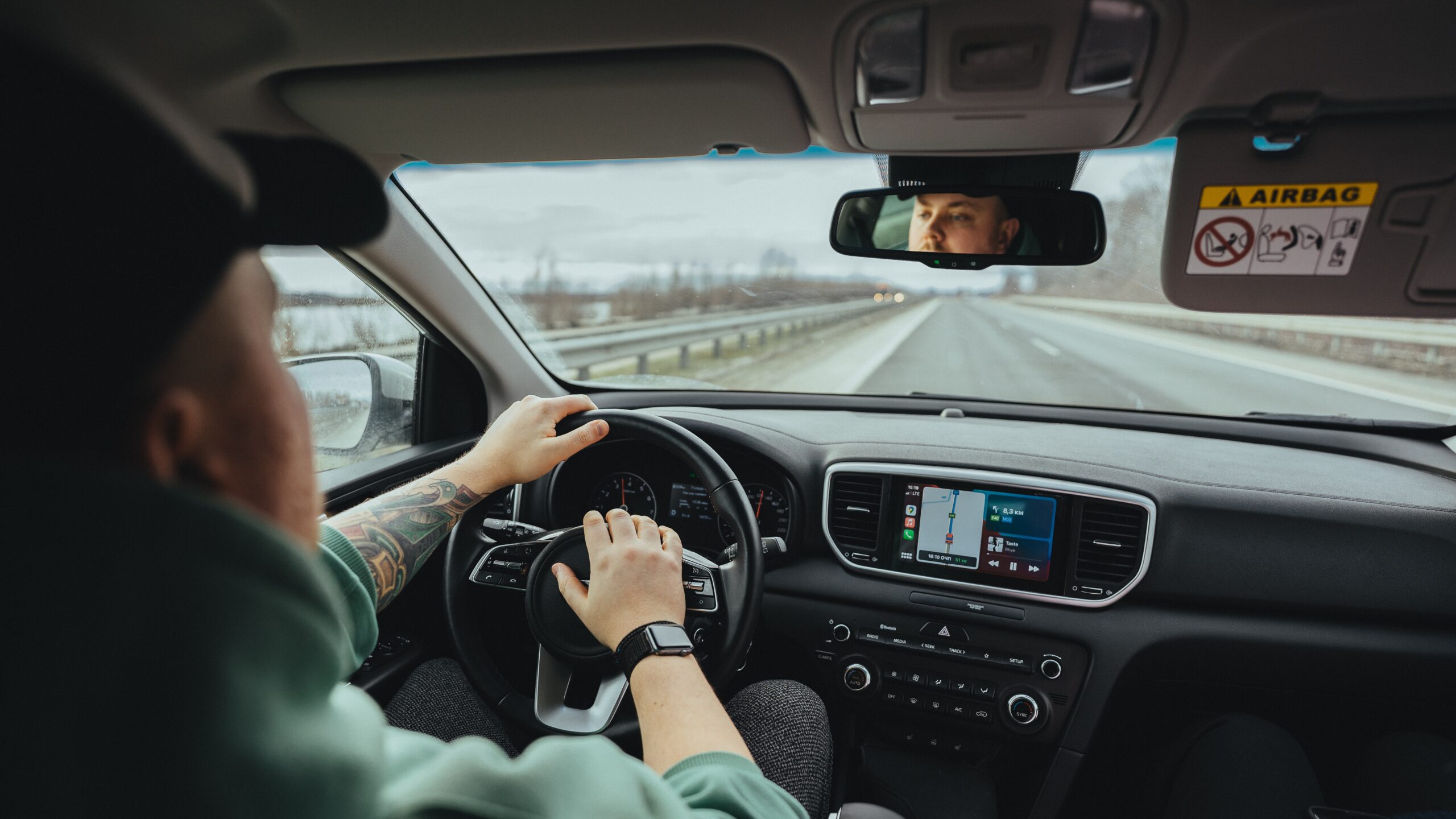 Man in a hat driving a car with his hand on the horn
