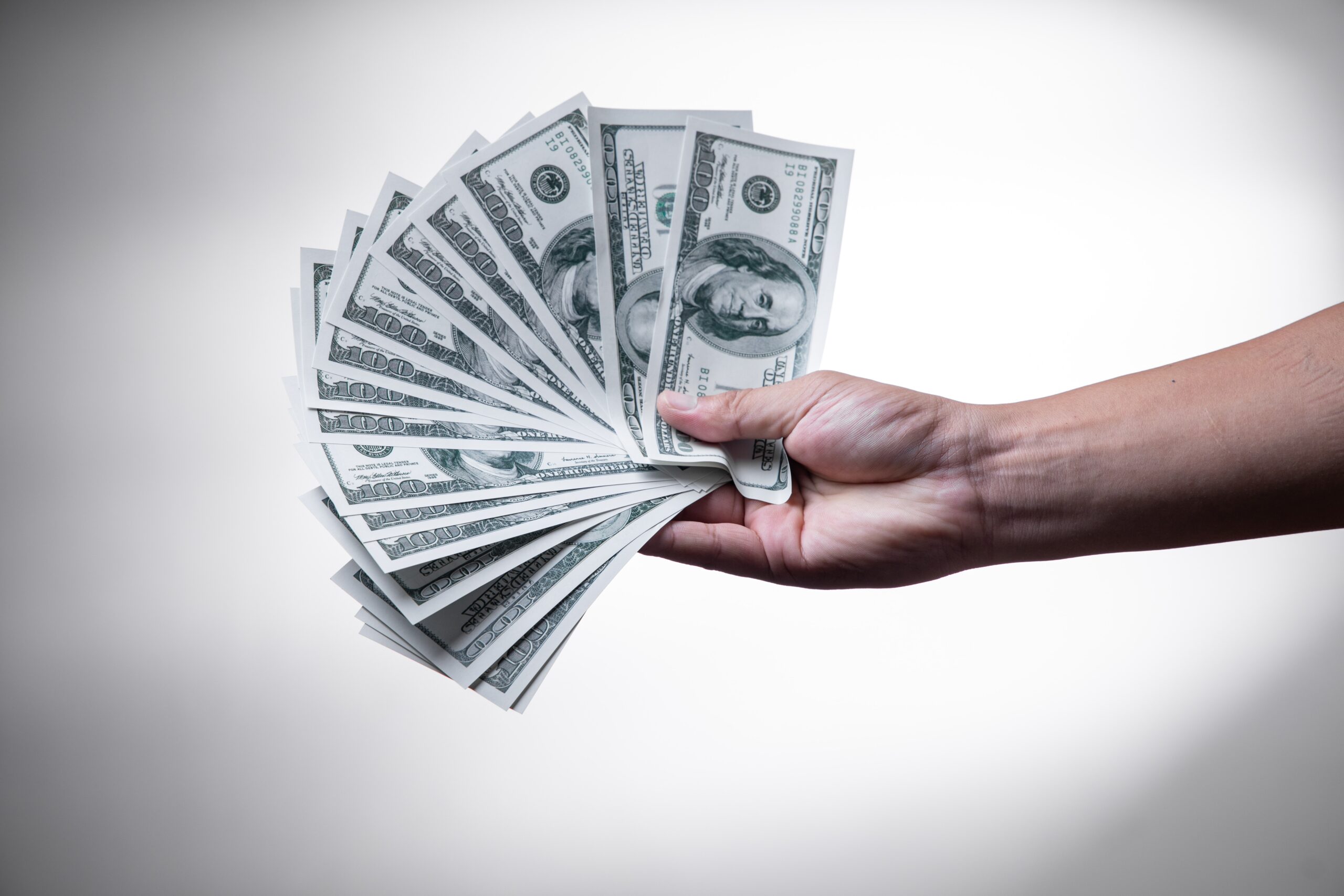 Person holding handful of fanned out hundred dollar bills