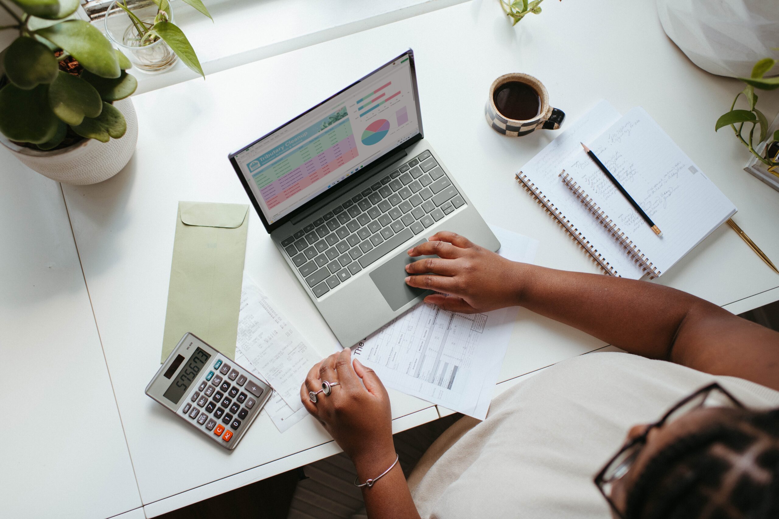 Person working on laptop surrounded by paper, calculator and pens