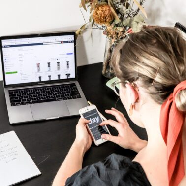 Woman with orange hire tie looking at phone while sitting in front of laptop