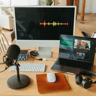Podcast set up on table with a laptop, mic, headphones, and desktop computer